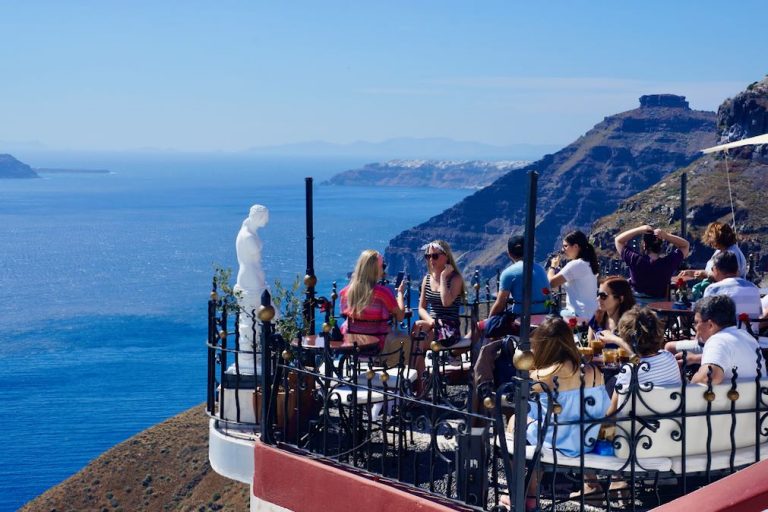 People enjoying a cold beverage and the Caldera view from a cliffside bar in Santorini